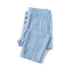 Light blue linen trousers folded flat, showing the rolled cuff and button-fly closure
