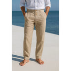 Man on a beach wearing khaki linen trousers with a white linen shirt, front view