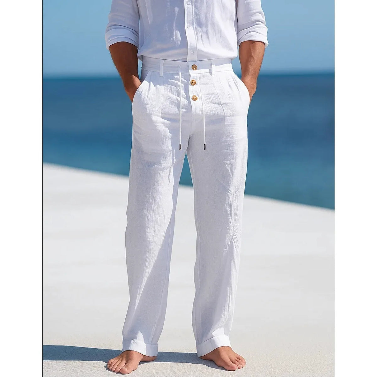 Man on a beach wearing white linen trousers with a white linen shirt, close-up front view