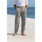 Man on a beach wearing grey linen trousers with a white linen shirt, front view