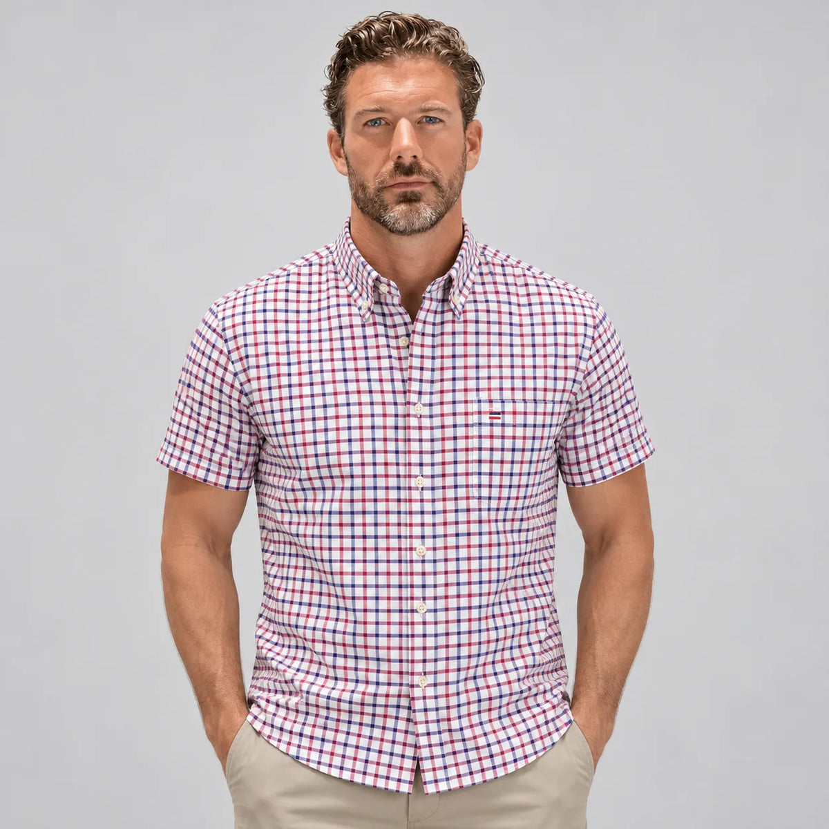 Front view of a man wearing a short-sleeve check shirt in red, navy and white with a buttoned chest pocket