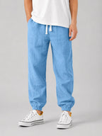 Front view of man wearing light blue textured linen jogger trousers with white drawstring waist and white sneakers