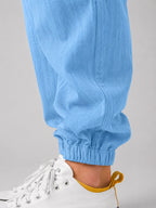 Close-up of light blue linen trouser leg showing elasticated cuff above white and yellow sneaker