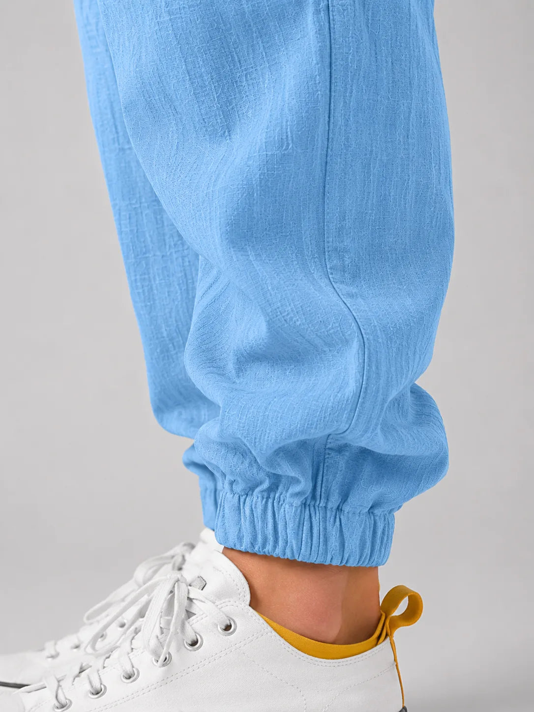 Close-up of light blue linen trouser leg showing elasticated cuff above white and yellow sneaker
