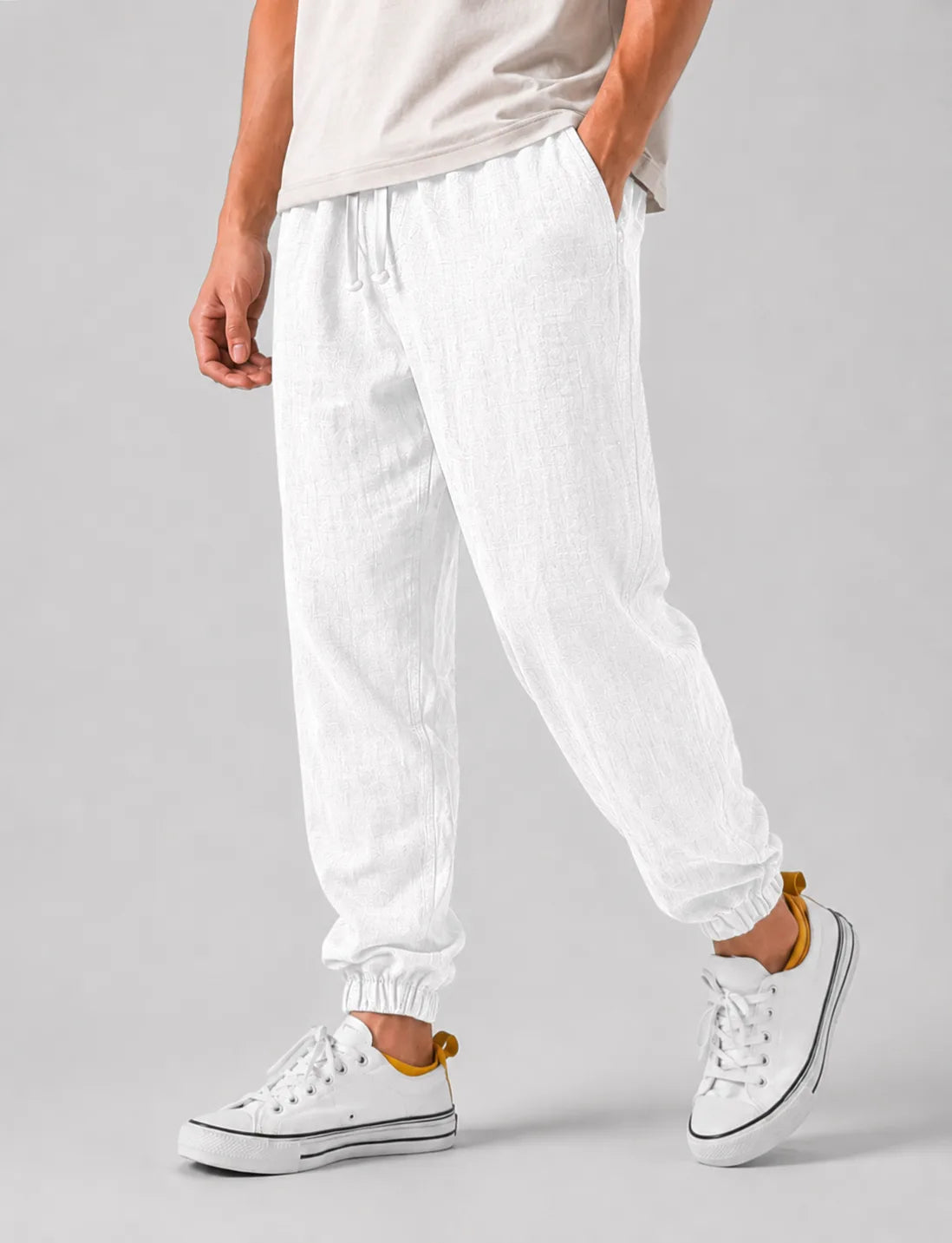 Side view of white textured linen jogger trousers with drawstring waist paired with white sneakers