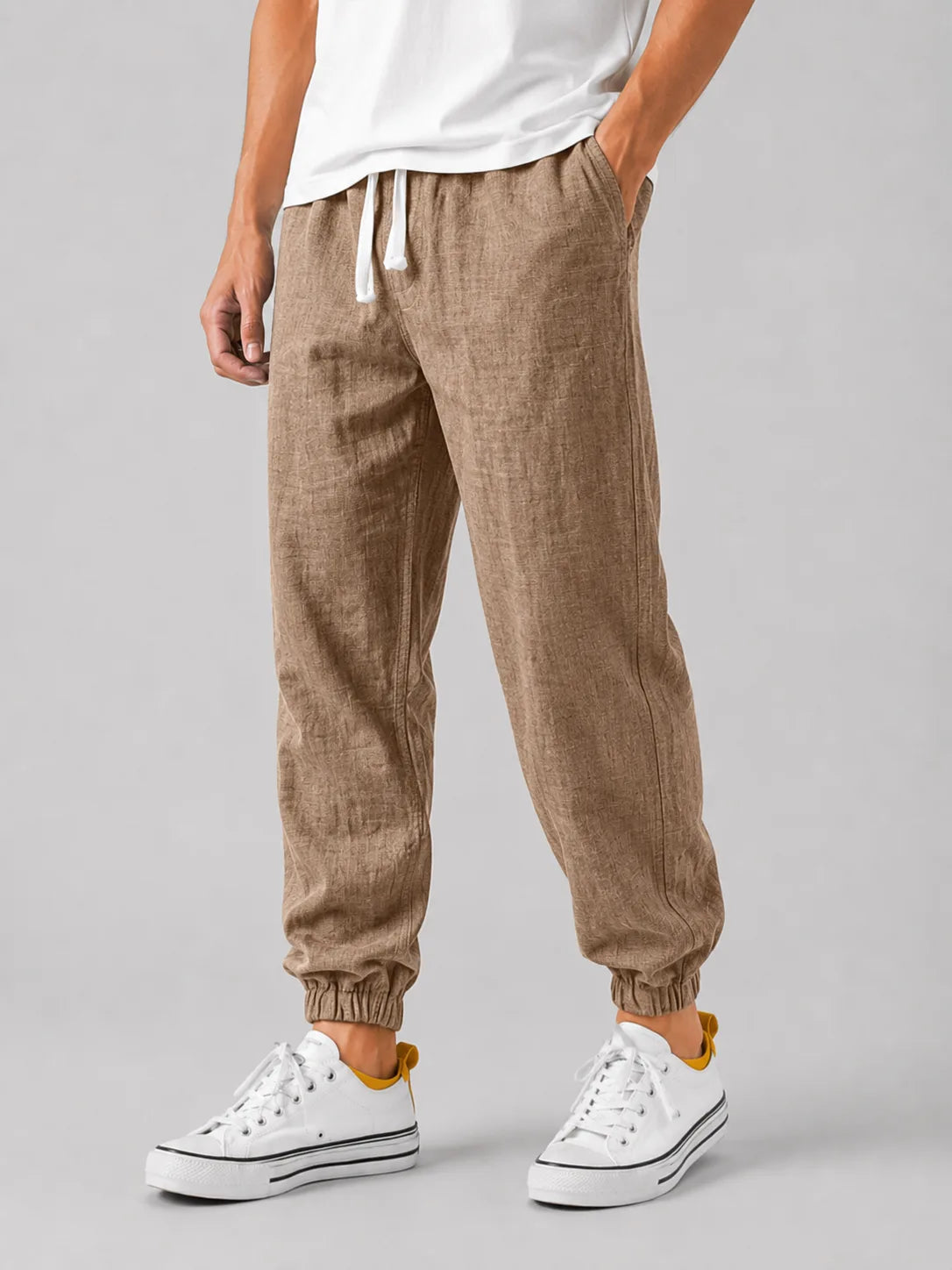 Side view of khaki brown textured linen jogger trousers with elasticated cuffed ankle and white sneakers