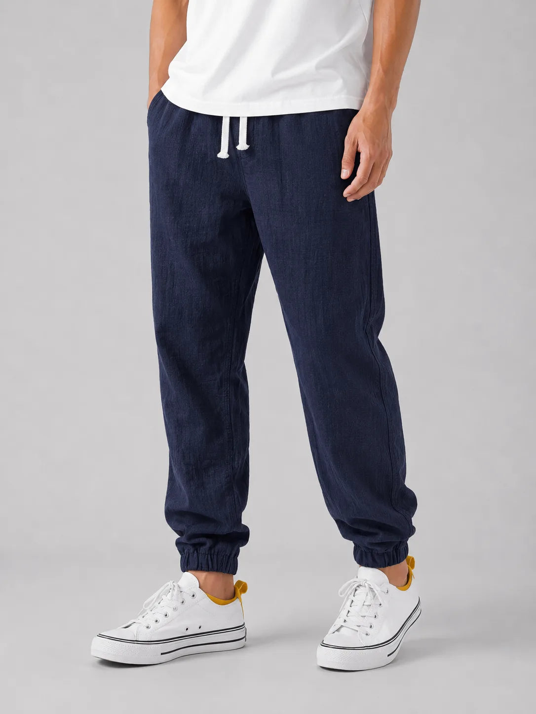 Front angled view of navy blue linen jogger trousers with white drawstring and elasticated ankle cuff