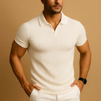 Close-up of a man wearing a cream ribbed knit polo with open collar and short sleeves, hands in white trouser pockets