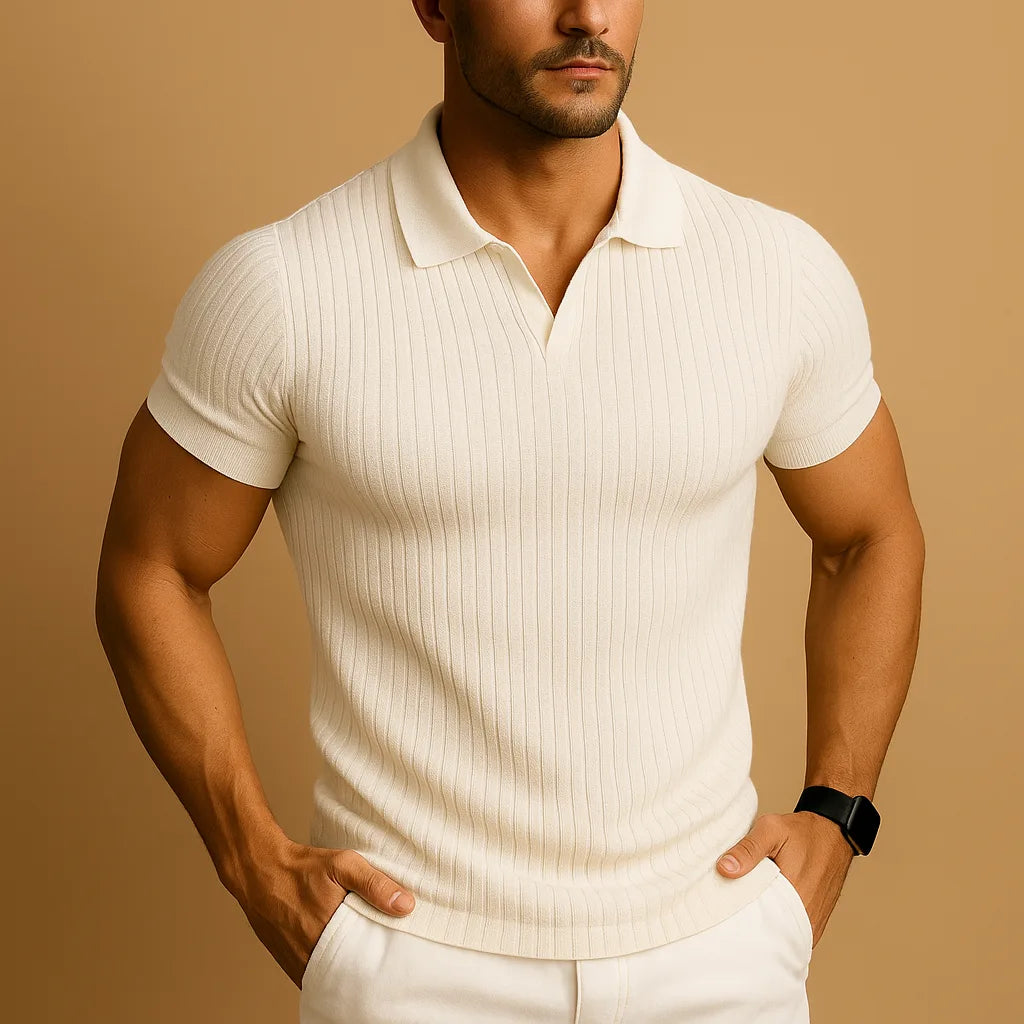 Close-up of a man wearing a cream ribbed knit polo with open collar and short sleeves, hands in white trouser pockets