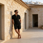 Man wearing the grey polo and shorts set with hands in pockets, side angle near stone wall