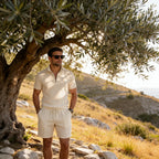 Man wearing the cream polo and shorts set standing under an olive tree on a sunlit hillside