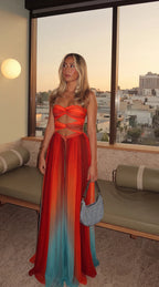 Full-length front view at sunset showing the sweetheart knot neckline, waist cutouts and flowing hemline against a city skyline.