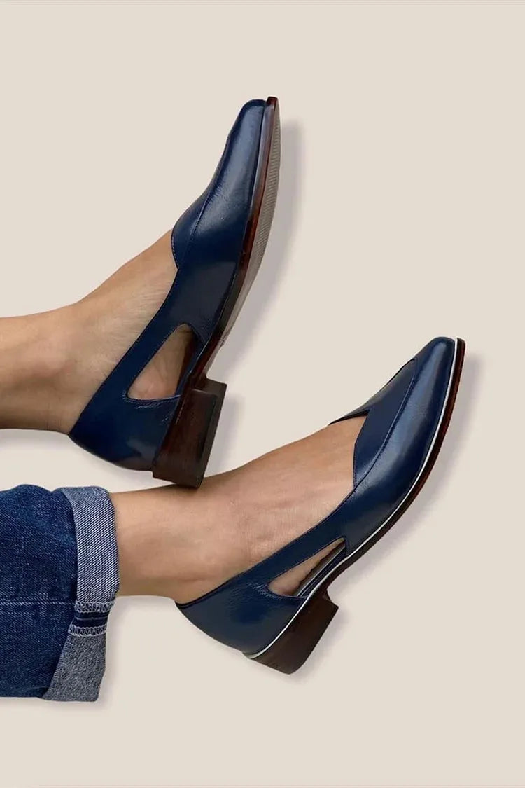Top-down view of navy leather flats showing the pointed toe, side cut-out and stacked wooden heel against a neutral backdrop