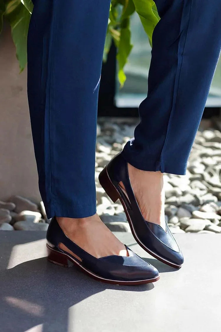 Navy leather flats worn outdoors with navy trousers, standing on a stone paved surface in natural sunlight