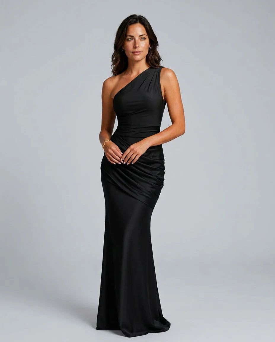 Woman in black one-shoulder satin maxi dress with draped waist, standing front-on in studio