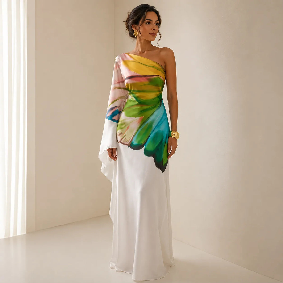 Front view of a model wearing a one-shoulder white maxi dress with a draped sleeve featuring a hand-painted multicolour print across the bodice.