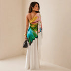 Back view showing the one-shoulder neckline and flowing draped sleeve, with the colourful print cascading over the shoulder onto the flowing skirt.