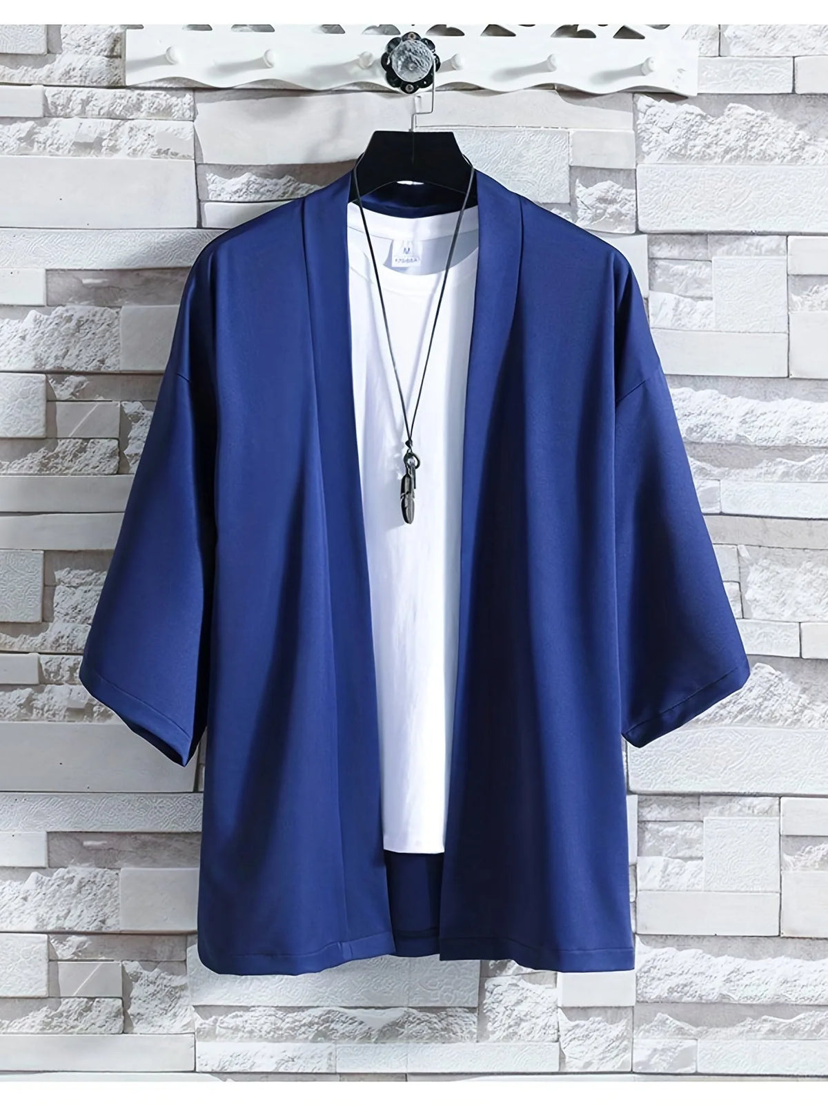 Navy blue kimono-style top with wide sleeves hanging on a wooden hanger against a stone wall