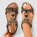 Top-down view of black and tan sandals with braided straps, beaded band and butterfly charm