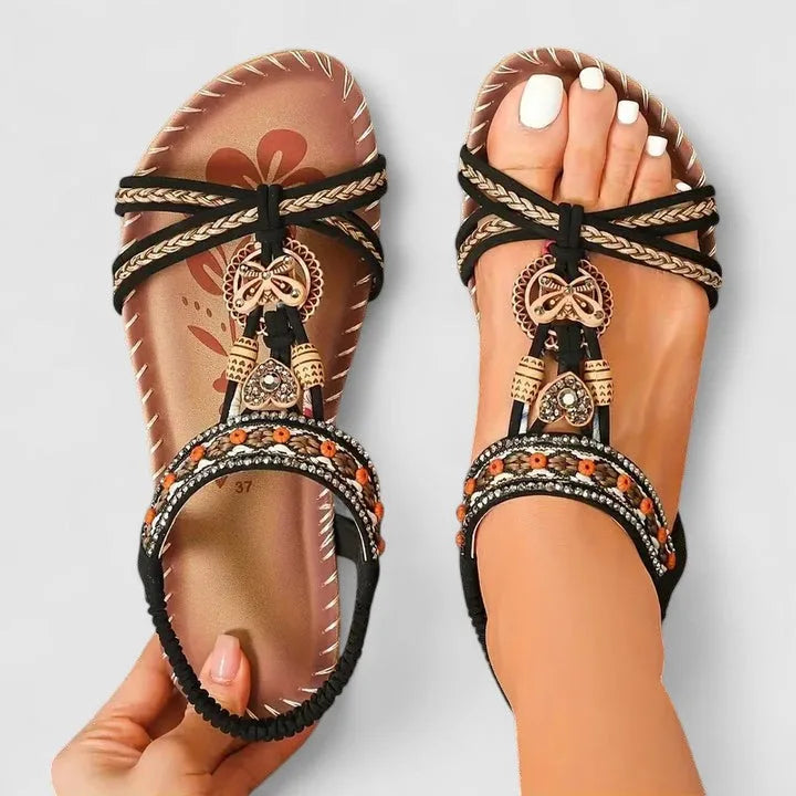 Top-down view of black and tan sandals with braided straps, beaded band and butterfly charm
