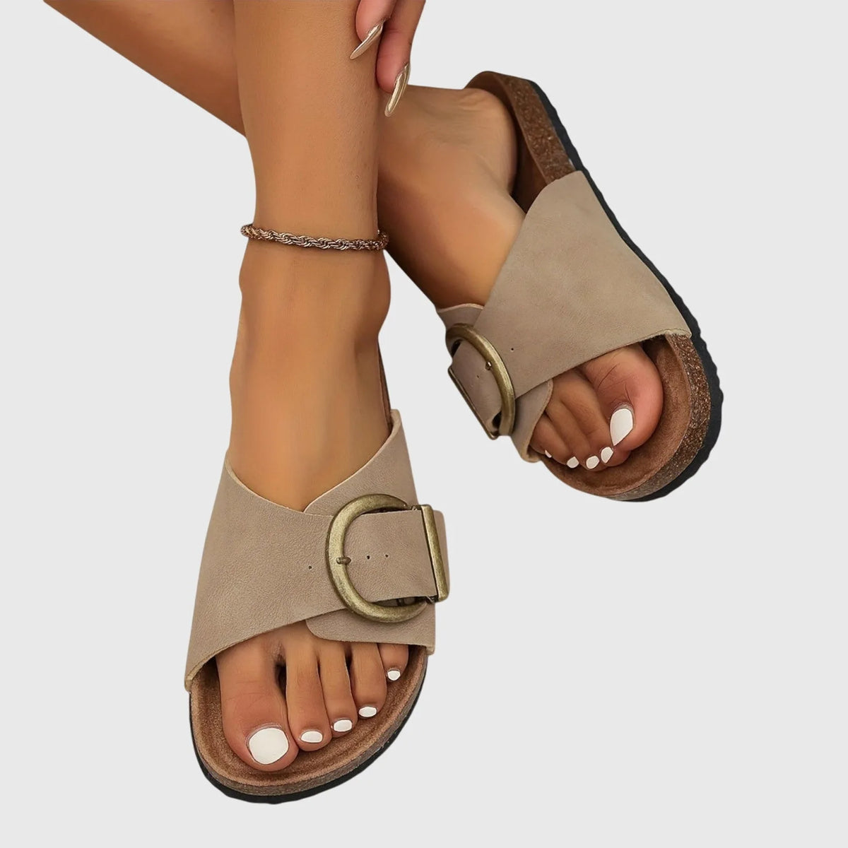 Taupe suede-look sandals with crossover strap and gold buckle, worn on feet in a close-up ankle shot