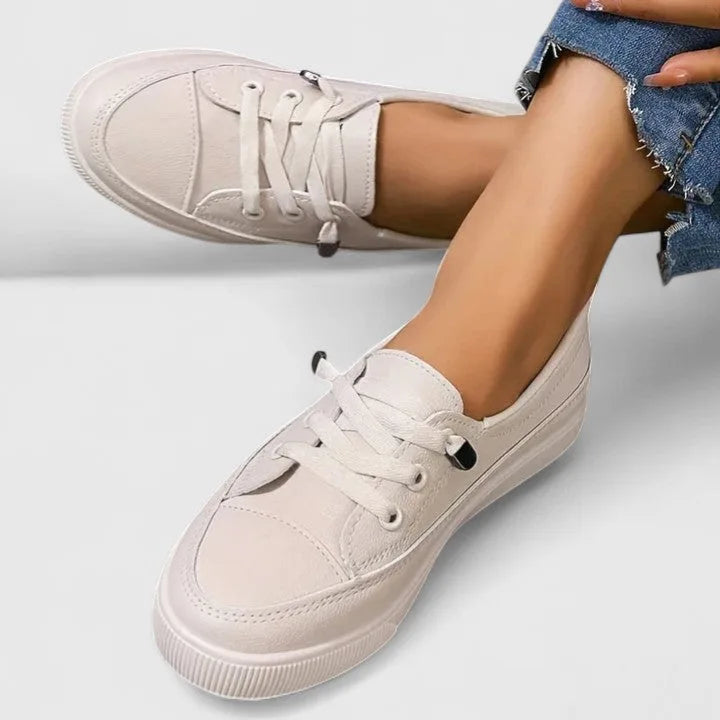 Top-down view of beige lace-up sneakers on crossed feet, showing smooth upper and ridged platform sole
