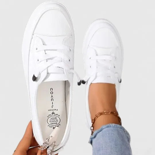 Overhead view of a pair of white sneakers held by hand, showing branded insole and lace-up fastening