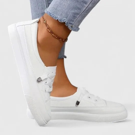 Close side profile of white sneaker on foot against a plain background, showing toe seam and sole thickness