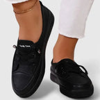 Side view of black lace-up sneakers worn with rolled denim jeans, showing platform sole from heel angle