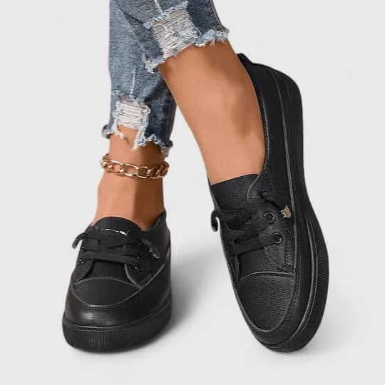 Front view of black lace-up sneakers on both feet with white denim, showing printed heel tab detail
