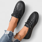 Close-up front angle of black sneakers on feet, showing lace pattern and rounded toe box