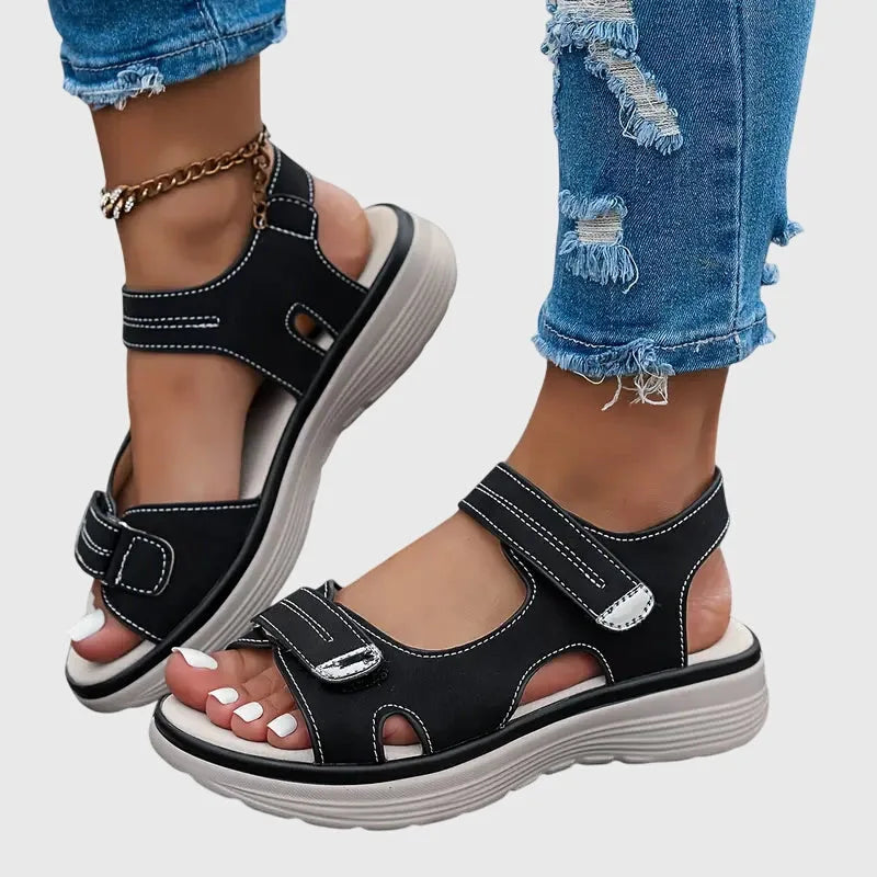 Side view of black sandal with touch-strap straps, white stitching detail and chunky ridged sole, worn on foot