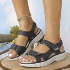Pair of black ankle-strap comfort sandals with cut-out sides shown on a wooden log outdoors