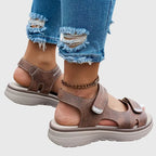 Brown sandal worn on foot, side view showing touch-strap ankle closure and ridged wedge sole