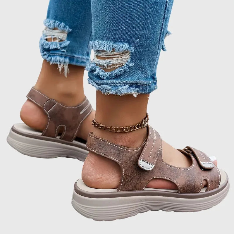 Brown sandal worn on foot, side view showing touch-strap ankle closure and ridged wedge sole