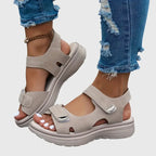 Close-up of brown sandals held in hand, showing textured upper and adjustable toe strap detail