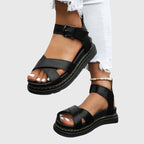 Black crisscross-strap platform sandal shown from the side, worn with a cropped ankle and contrast stitching on the sole