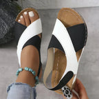 Hand holding black and white T-strap sandal beside a matching sandal worn on bare foot