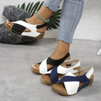 Hand lifting a navy and white wedge sandal to show the stitched outsole and arch shape