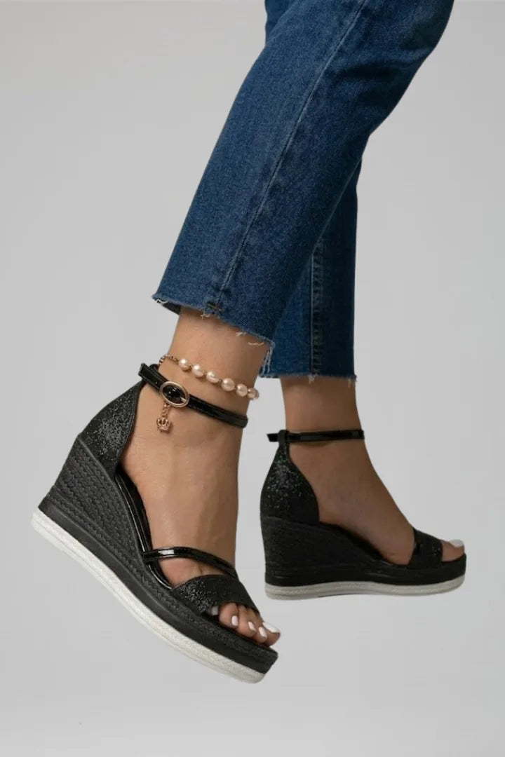 Side view of black glitter wedge sandal showing woven platform sole and gold buckle ankle strap detail