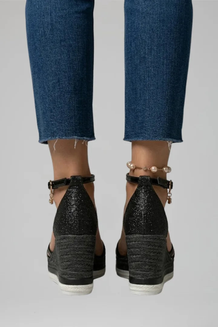 Back view of both black glitter wedge sandals showing woven heel counter and white contrast midsole