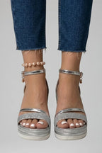 Front close-up of feet in silver metallic wedge sandals with glitter strap and pearl anklet accessory