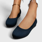 Front view of feet wearing navy blue knit ballet flats with an ankle bracelet accessory