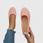 Pair of pink knit ballet flats shown from above, one held in hand to display a decorative pearl clip