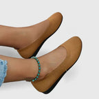 Close-up of feet wearing tan knit ballet flats with a turquoise beaded anklet