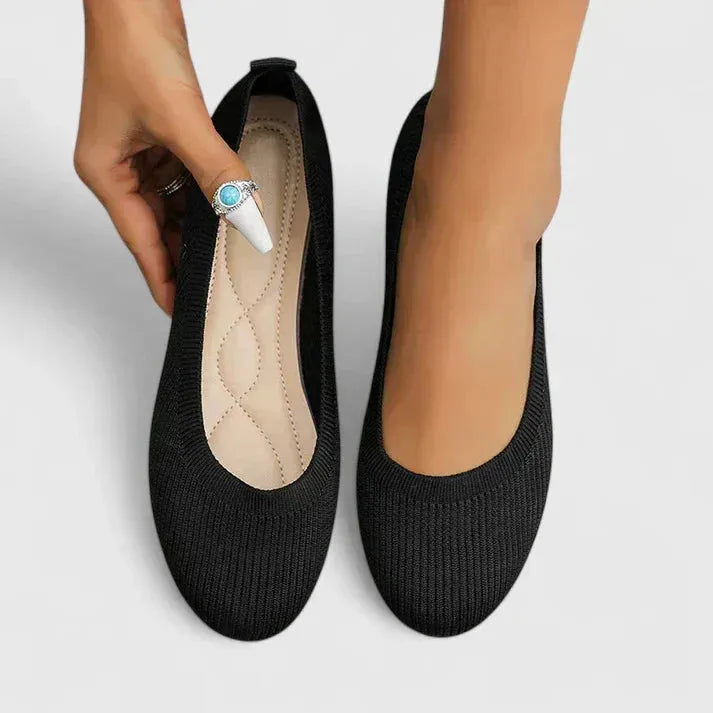 Overhead view of black knit ballet flats on feet, showing the quilted beige insole detail