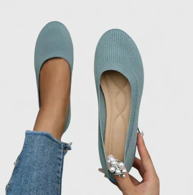 Pair of light blue knit ballet flats displayed upright, one held to show the stitched inner sole