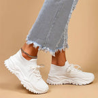 Side view of a white knit sneaker worn on foot with ripped denim jeans, showing the sock-like fit and lace-up front