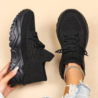 Overhead shot of a hand holding a black knit sneaker next to its pair worn on foot, highlighting the all-black chunky platform sole