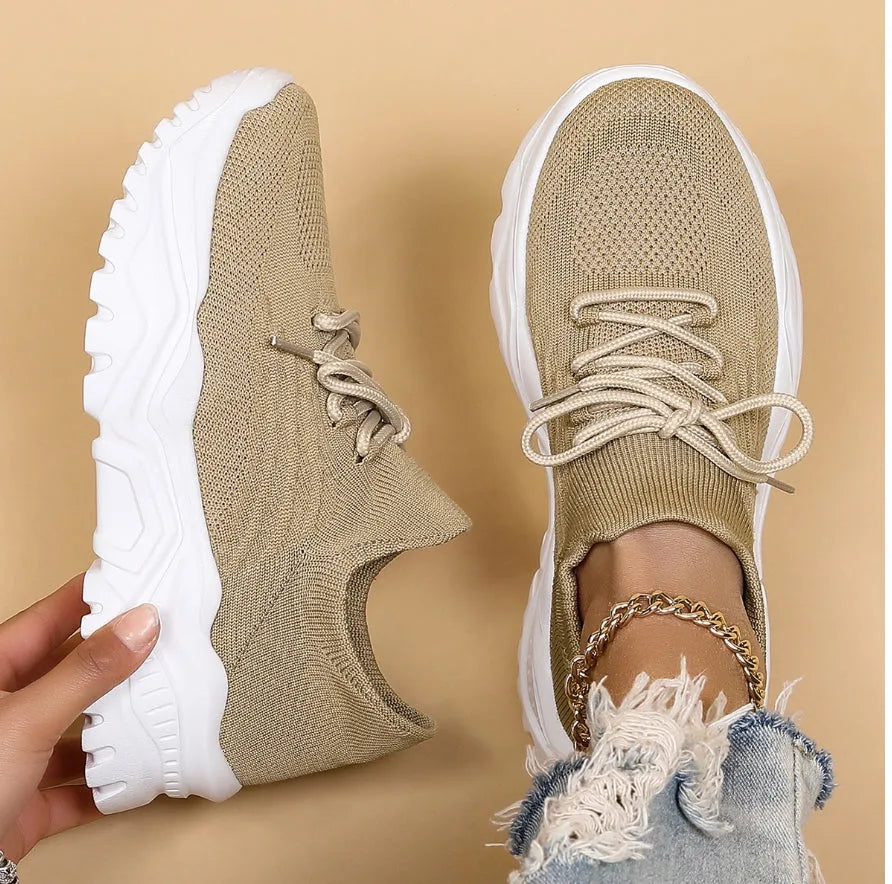 Side-by-side view of a beige knit sneaker with white chunky sole, one held by hand and one worn on foot with ripped jeans